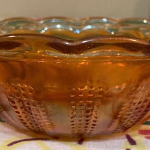 May include: A vintage amber glass bowl with a scalloped rim and a textured design. The bowl is made of iridescent glass and has a warm, inviting color.