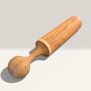 Könnte beinhalten: Ein hellbrauner Holzstößel mit rundem Griff und zylindrischem Körper. Der Stößel ist aus Naturholz gefertigt und weist einen Riss entlang des Körpers auf. Dieses Küchenwerkzeug wird zum Mischen von Zutaten in Cocktails und anderen Getränken verwendet.