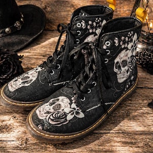 May include: Black lace-up boots with a skull and floral design. The boots feature a brown sole with yellow stitching and eyelets. The skull and floral design is in shades of gray and white.