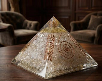 May include: A clear pyramid-shaped object with a copper coil and gold glitter accents. The pyramid is filled with clear crystals and sits on a dark wooden surface. The design features a spiral and coil pattern.