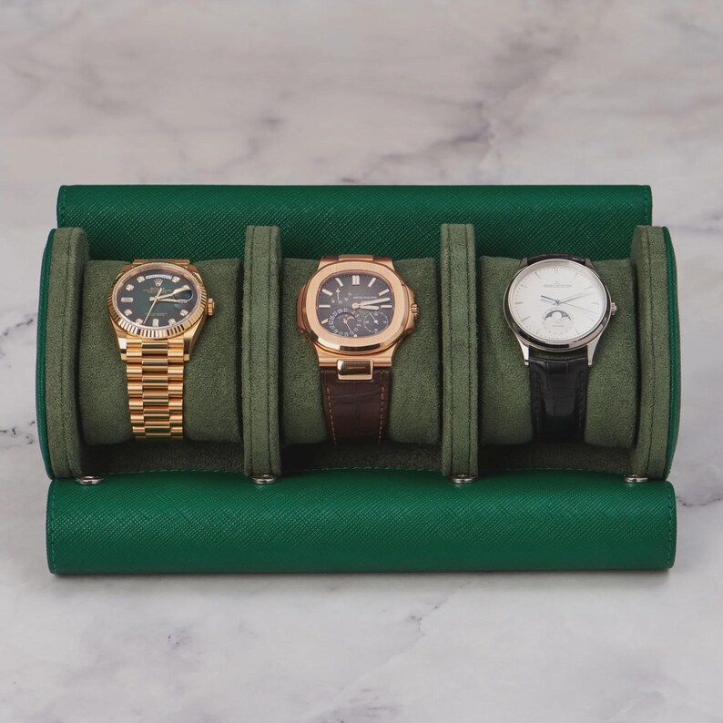 May include: A green leather watch travel case holding three luxury watches. The watches include a gold watch with a green face, a rose gold watch with a brown leather strap, and a silver watch with a black leather strap.