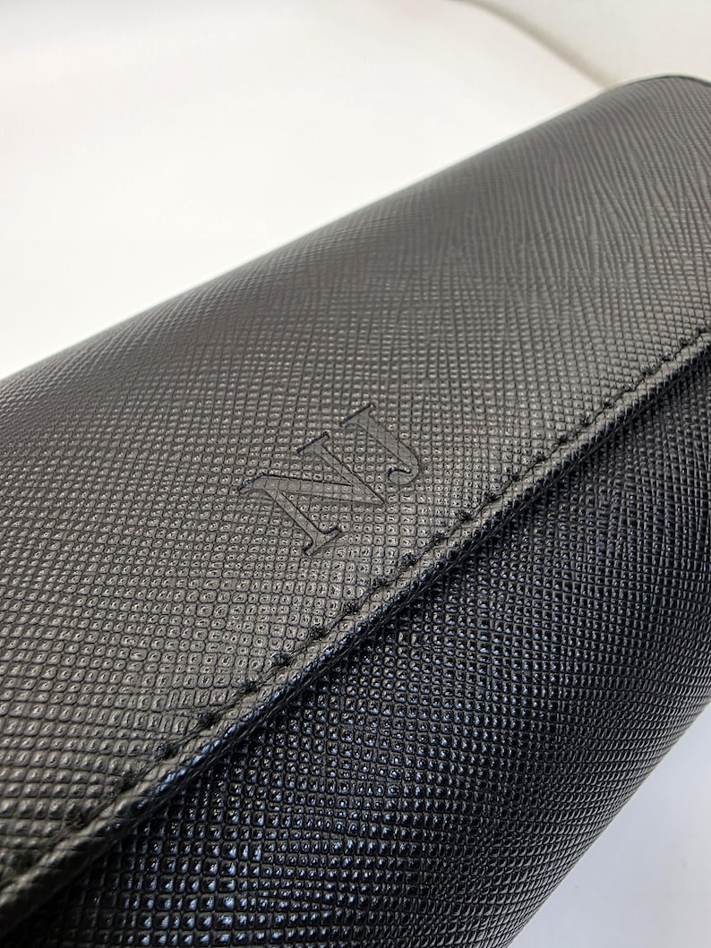 May include: Close-up of a black leather wallet with a textured pattern. The wallet has a flap closure and the initials "NJ" embossed on the front. The stitching is visible along the edges.
