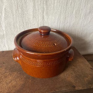 May include: A brown ceramic casserole dish with a lid. The dish has two handles and a decorative dotted pattern around the rim and on the lid. The lid has a small knob on top.