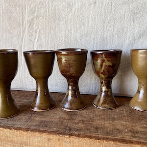 May include: A white ceramic mug with a black handle and the text "But First, Coffee" in a handwritten style. The mug is on a white surface. The mug is approximately 10 cm tall.