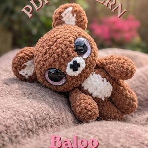 May include: A brown crocheted teddy bear with large black eyes, white inner ears, and a white chest patch. The bear has a small black cross-shaped nose. Text on the image reads: PDF PATTERN, Baloo, the cutest teddy bear, and @brin.de.miel2.