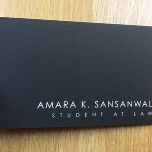 K&ouml;nnte beinhalten: Eine schwarze Visitenkarte mit wei&szlig;em Text, der "Amara K. Sansanwal, Student at Law." lautet.