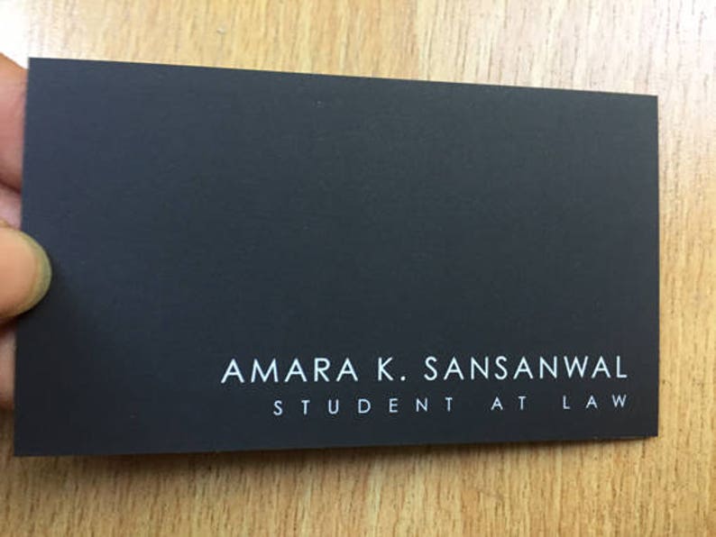 K&ouml;nnte beinhalten: Eine schwarze Visitenkarte mit wei&szlig;em Text, der "Amara K. Sansanwal, Student at Law." lautet.