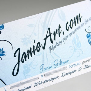 K&ouml;nnte beinhalten: Eine rechteckige Visitenkarte mit abgerundeten Ecken, hellblauem Hintergrund und dunkelblauen Blumenmotiven. Der Text lautet JanieArt.com, Marking your presence on the web, Janie Giltner, Portfolio.janieart.com und Professional Web developer, Designer & Illustrator.