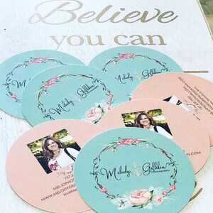 Puede incluir: Tarjetas de visita redondas para Melody Gillikin Photography con un lado turquesa con un logotipo de corona floral y un lado color melocot&oacute;n con un retrato, datos de contacto y la direcci&oacute;n web. El texto Believe you can es visible.