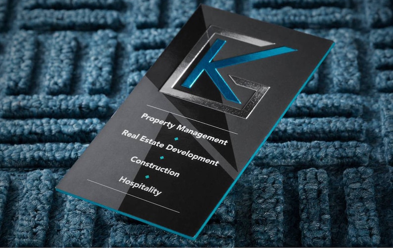 May include: Black business card with a silver embossed letter K in a blue square. The card lists services offered: Property Management, Real Estate Development, Construction, Hospitality.