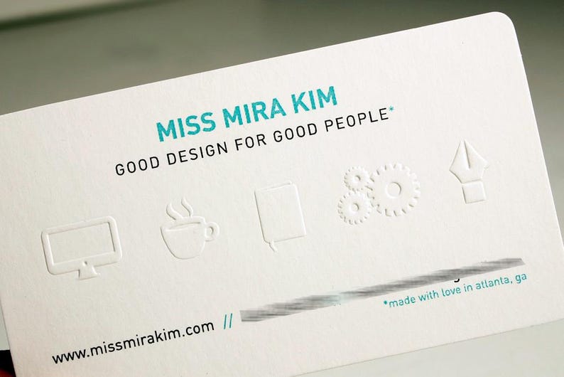 May include: A white business card with the text "MISS MIRA KIM" in teal, followed by "GOOD DESIGN FOR GOOD PEOPLE." Embossed icons include a computer monitor, coffee cup, notebook, gears, and a pen nib. The website address is visible at the bottom.