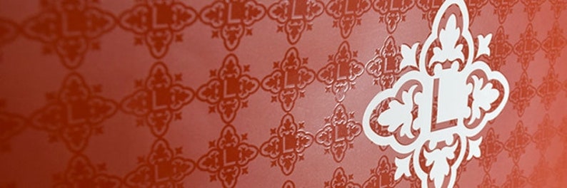 May include: A vibrant red surface featuring a repeating pattern of dark red, stylized cross-shaped motifs, each containing the letter L. A large, white, ornate, symmetrical emblem featuring a central letter L is positioned on the right side.