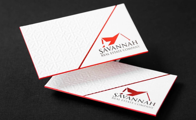 May include: Two white rectangular business cards with red edges. The cards feature a textured geometric pattern on the left and a red logo with the text SAVANNAH REAL ESTATE COMPANY on the right, separated by a diagonal red line.