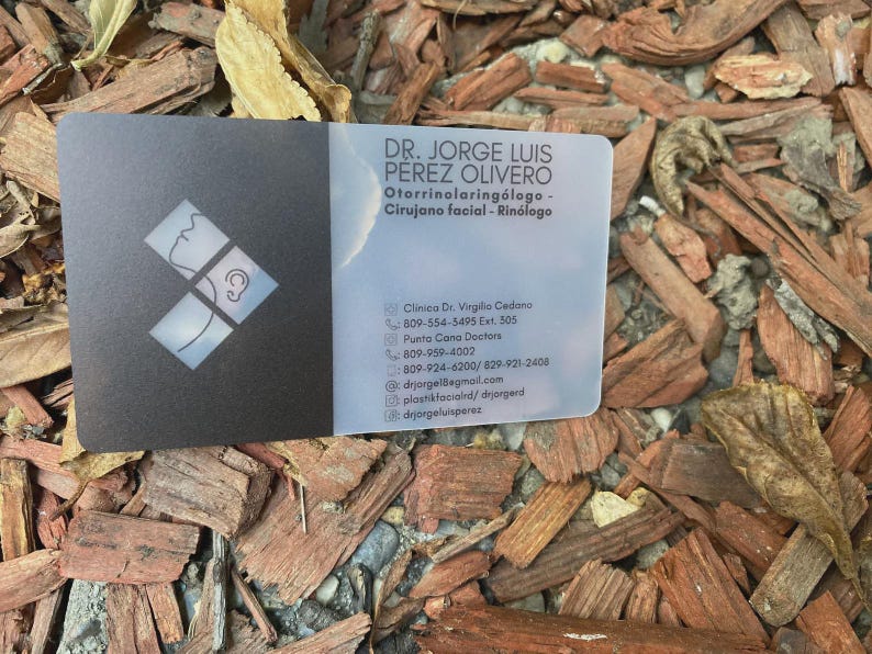 May include: A rectangular business card with a matte black left side featuring a white geometric logo of a profile and ear, and a translucent right side with black text for Dr. Jorge Luis Perez Olivero, Otorrinolaringologo, and contact details.
