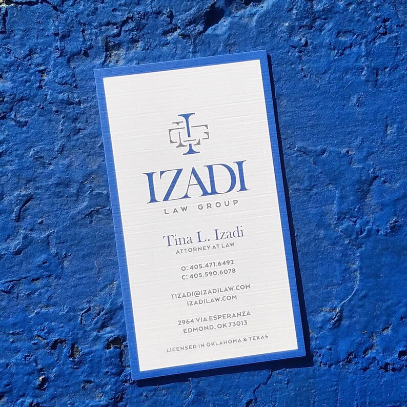 May include: A white business card with blue trim. The card features the text "IZADI LAW GROUP" and the name "Tina L. Izadi, Attorney at Law". The card also includes contact information, including a phone number, email address, and website address. The card lists the address "2964 Via Esperanza, Edmond, OK 73013" and states that the law firm is licensed in Oklahoma and Texas.