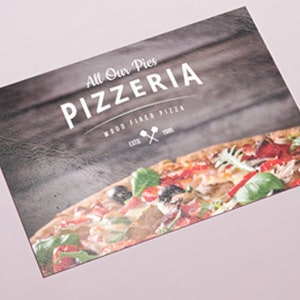 May include: A rectangular menu card featuring a dark wood grain background with the white text All Our Pies PIZZERIA WOOD FIRED PIZZA ESTD 1985 and a small icon of two crossed pizza peels. The bottom portion displays a colorful pizza with toppings.