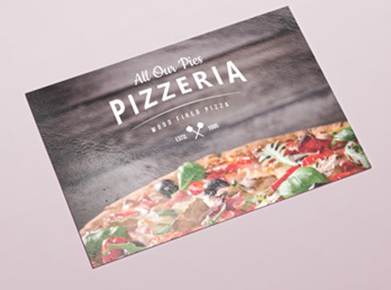 May include: A rectangular menu card featuring a dark wood grain background with the white text All Our Pies PIZZERIA WOOD FIRED PIZZA ESTD 1985 and a small icon of two crossed pizza peels. The bottom portion displays a colorful pizza with toppings.