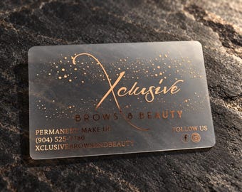 Könnte beinhalten: Eine rechteckige, halbtransparente, mattierte Visitenkarte mit kupferfarbenem Text und Grafiken. Die Karte zeigt den Text Xclusive BROWS & BEAUTY, PERMANENT MAKE UP, (904) 525-7780, FOLLOW US und XCLUSIVEBROWSANDBEAUTY sowie Social-Media-Symbole.