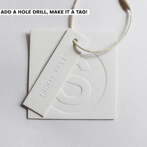 May include: White tag with the text "STYLE VOGUE" embossed on a rectangular tag, with a square tag behind it. The square tag has a large "S" embossed on it. The text "ADD A HOLE DRILL, MAKE IT A TAG!" is at the top.