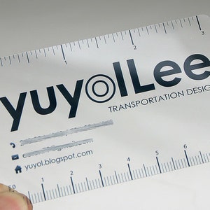 Puede incluir: Una tarjeta de visita rectangular de pl&aacute;stico transl&uacute;cido con una regla en los bordes superior e inferior. El borde superior mide hasta 3 pulgadas y el inferior hasta 8 cent&iacute;metros. El texto dice yuyolLee TRANSPORTATION DESIGN.