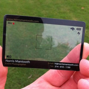 Puede incluir: Una tarjeta de visita rectangular transparente con bordes negros, dise&ntilde;ada para parecer un visor de c&aacute;mara. Muestra el texto Norris Mantooth, Event Photographer, el sitio web www.norrismantooth.com, el correo hi@norrismantooth.com y el tel&eacute;fono 214-810-1190.