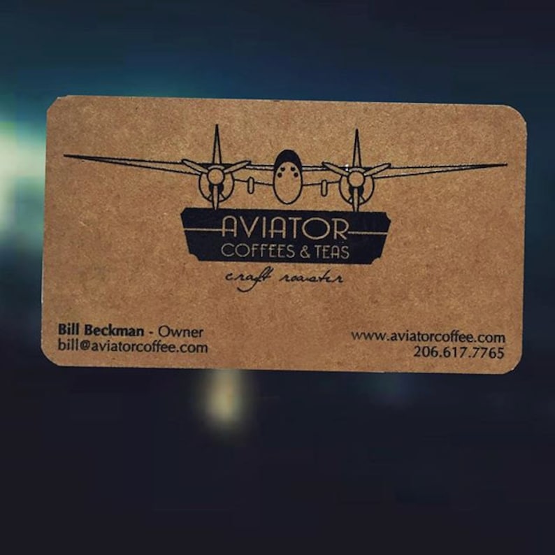May include: A rectangular business card with rounded corners. The card is a light brown color and features a black graphic of a vintage airplane above the words "AVIATOR COFFEES & TEAS craft roaster". The owner's name, email, and website are also printed on the card.