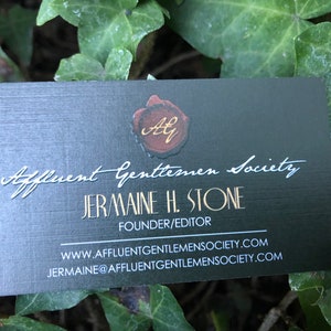 K&ouml;nnte beinhalten: Eine rechteckige schwarze Visitenkarte mit einem roten Wachssiegel-Motiv und goldenen Initialen AG oben. Der Text lautet Affluent Gentlemen Society, Jermaine H. Stone, Founder/Editor, inklusive Website und E-Mail-Adresse in wei&szlig;er Schrift.
