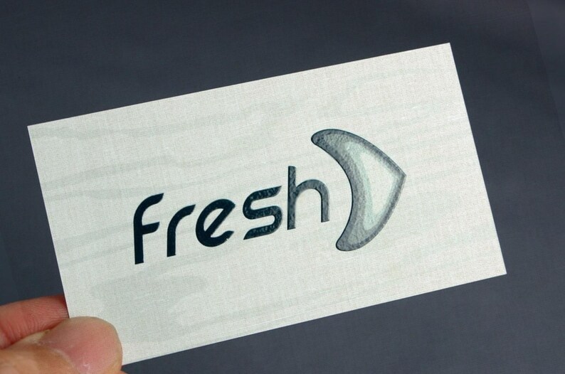 K&ouml;nnte beinhalten: Eine rechteckige wei&szlig;e Karte mit dem Wort fresh in dunkelblauen Kleinbuchstaben, gefolgt von einem stilisierten grauen Symbol in Form eines Bumerangs. Die Karte weist eine subtile horizontale Holzmaserung auf der gesamten Oberfl&auml;che auf.