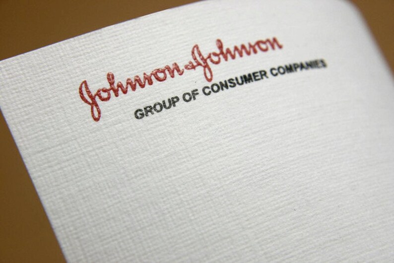 K&ouml;nnte beinhalten: Ein wei&szlig;es, strukturiertes Blatt Papier mit dem roten, kursiven Johnson & Johnson-Logo im oberen Bereich, wobei der schwarze Text GROUP OF CONSUMER COMPANIES direkt unter dem Logo in einer klaren, serifenlosen Gro&szlig;buchstabenschrift steht.