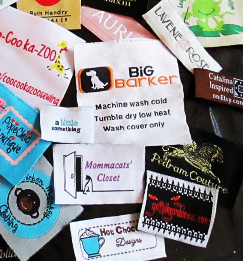 May include: A collection of various rectangular fabric clothing labels featuring diverse brand names and logos including Big Barker, Coo-ka-ZOO, PixieChic Boutique, Mommacats' Closet, Pedram Couture, and Hot Choco Designs with embroidered text and graphics.