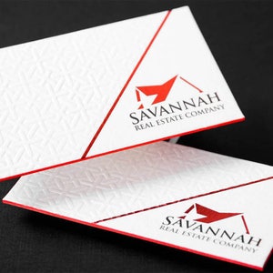 May include: Two white business cards with a red border and a red diagonal line. The cards feature a red house logo with the text "SAVANNAH REAL ESTATE COMPANY" in black.