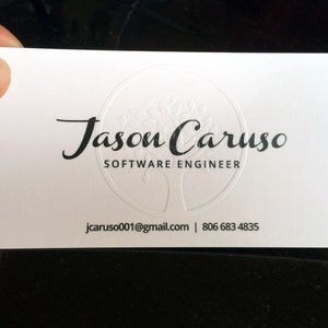 May include: A white business card with the name "Jason Caruso" and the title "Software Engineer" printed in black. The card also includes an email address and phone number. A tree design is embossed in the center.