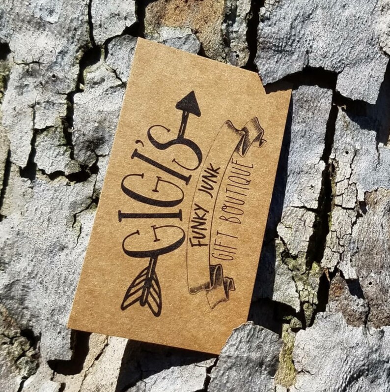 May include: A rectangular tan card with black ink printing. The text reads GIGI'S FUNKY JUNK GIFT BOUTIQUE. The design features a stylised arrow pointing upward through the word GIGI'S and a ribbon banner containing the words FUNKY JUNK GIFT BOUTIQUE.