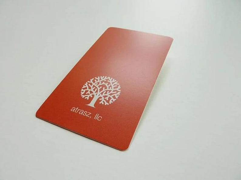 May include: A rectangular, terracotta-colored card with rounded corners. The card features a white graphic of a stylized tree with intricate branches and the text "atrasz, llc" printed in white below the tree icon on the front surface.
