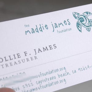 K&ouml;nnte beinhalten: Eine wei&szlig;e Visitenkarte mit dem Text the maddie james foundation in Blaugr&uuml;n, einer blaugr&uuml;nen Meeresschildkr&ouml;ten-Grafik und dem Namen COLLIE F. JAMES, TREASURER in Dunkelgrau. Die Karte enth&auml;lt eine Adresse in Capistrano Beach, CA 92624-0322.