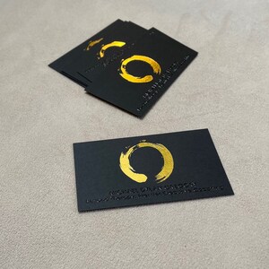 May include: A stack of rectangular black business cards and one single card placed in front. Each card features a gold foil-stamped circular brushstroke logo, with the text MICHAEL DYLAN GREGORY and BEYOND THERAPY: PREMIER EXECUTIVE COACHING printed below.