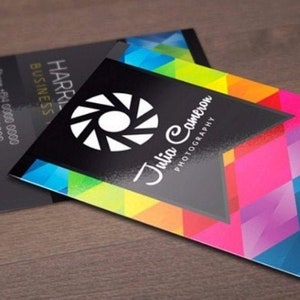 May include: Two rectangular business cards featuring a vibrant, multi-colored geometric pattern of triangles in shades of blue, pink, yellow, and green. One card displays a white camera shutter icon and the text Julia Cameron Photography.
