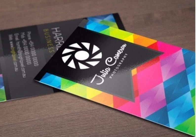 May include: Two rectangular business cards featuring a vibrant, multi-colored geometric pattern of triangles in shades of blue, pink, yellow, and green. One card displays a white camera shutter icon and the text Julia Cameron Photography.
