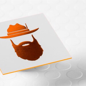 May include: A square white card featuring a metallic orange graphic of a wide-brimmed hat positioned above a thick, full beard. The card has a thin orange edge, and the design is centered on the flat surface of the white card stock.