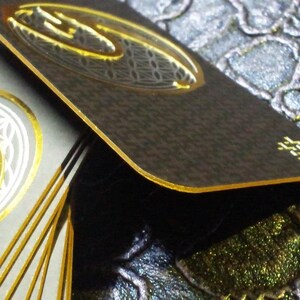 May include: A stack of black and gold business cards with a geometric design and gold foil accents. The cards are stacked on a textured surface.