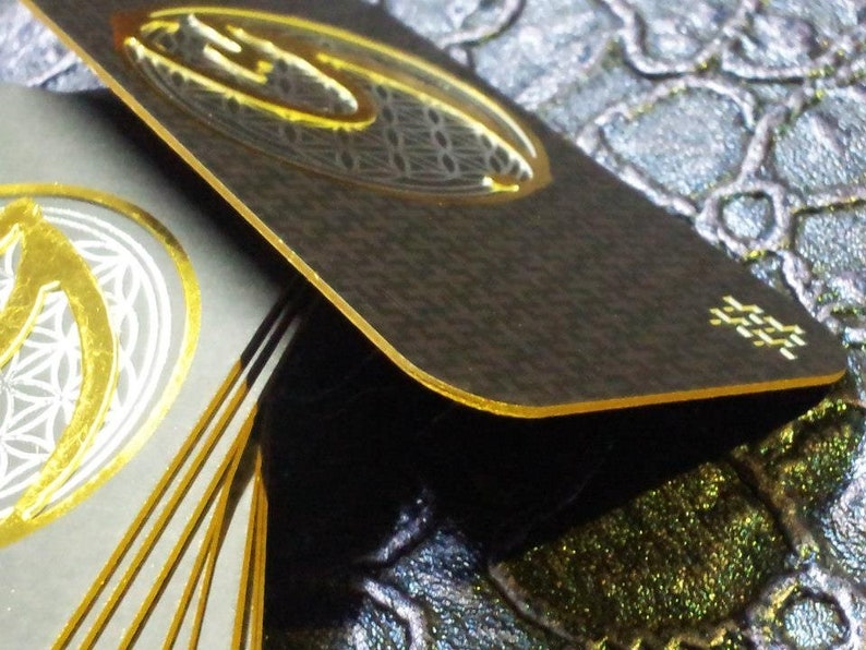 May include: A stack of black and gold business cards with a geometric design and gold foil accents. The cards are stacked on a textured surface.