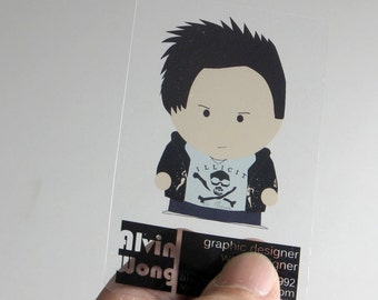 May include: A rectangular, semi-transparent business card featuring a cartoon character with spiky black hair, a black jacket, and a white t-shirt with a skull and crossbones graphic. The text reads Alvin Wong, graphic designer.