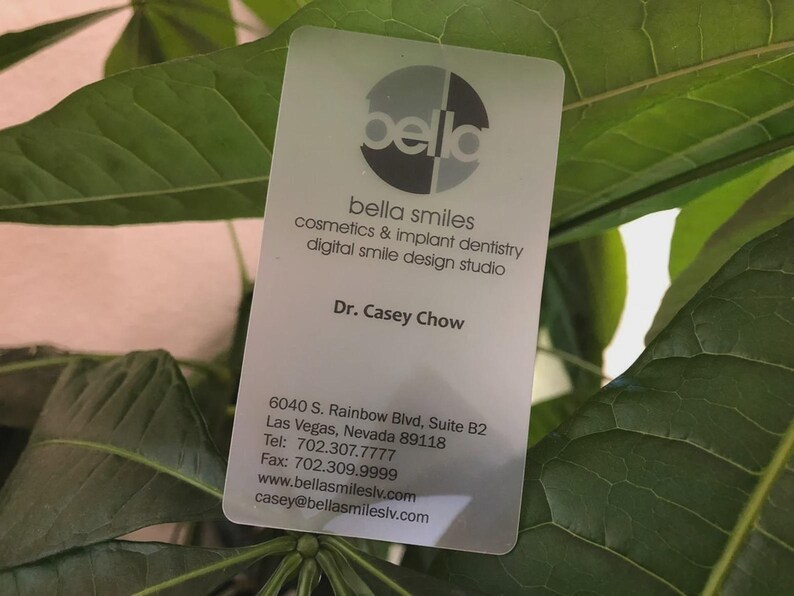 May include: A rectangular, semi-translucent business card for Bella Smiles, featuring a circular logo, the name Dr. Casey Chow, and contact details including the address 6040 S. Rainbow Blvd, Suite B2, Las Vegas, Nevada 89118, phone, fax, and email.