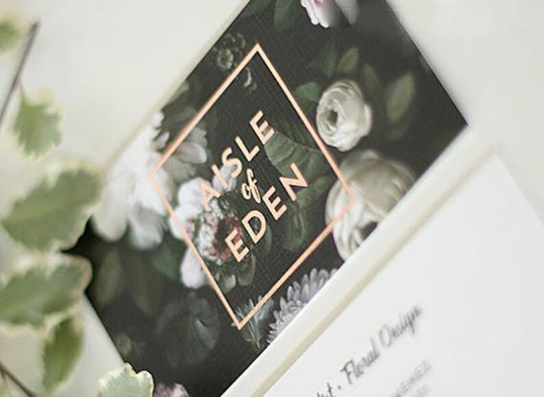 May include: A black and white floral design with a copper square overlay that says "AISLE of EDEN".