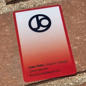 Może przedstawiać: Wizyt&oacute;wka w kolorze czerwonym i białym z czarnym k&oacute;łkiem zawierającym litery "JO" w lewym g&oacute;rnym rogu. Tekst "Juan Ortiz | Graphic Design" jest wydrukowany czarnym kolorem na dole wizyt&oacute;wki, wraz z numerem telefonu i adresem e-mail.