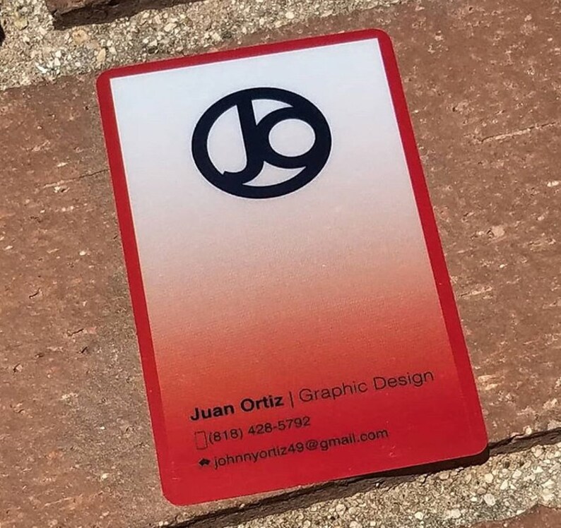 Może przedstawiać: Wizyt&oacute;wka w kolorze czerwonym i białym z czarnym k&oacute;łkiem zawierającym litery "JO" w lewym g&oacute;rnym rogu. Tekst "Juan Ortiz | Graphic Design" jest wydrukowany czarnym kolorem na dole wizyt&oacute;wki, wraz z numerem telefonu i adresem e-mail.