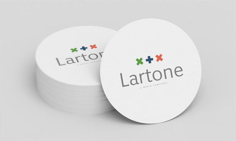 Puede incluir: Una pila de posavasos circulares blancos con el logotipo de Lartone en texto gris y un s&iacute;mbolo de cruz verde, azul oscuro y rojo encima. El texto debajo del logo dice A MEDIA COMPANY en letras may&uacute;sculas peque&ntilde;as de color gris.
