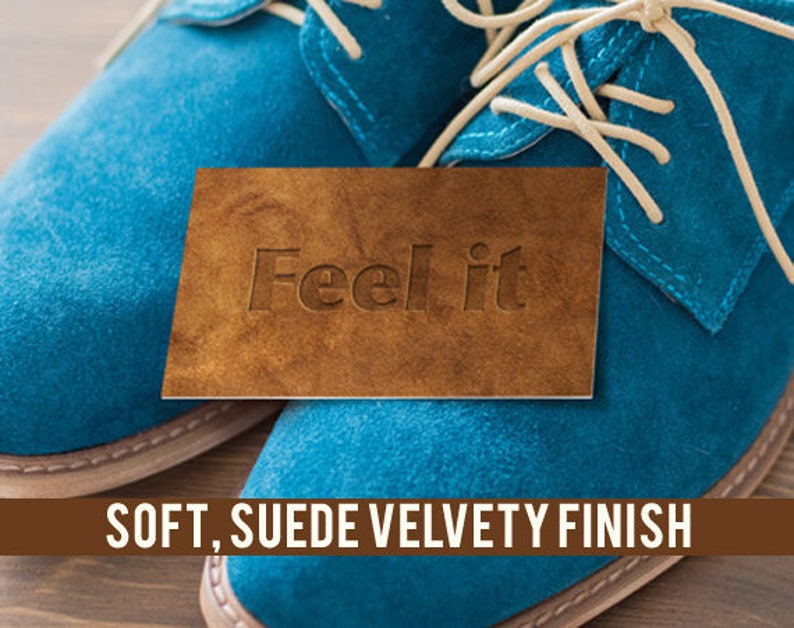 K&ouml;nnte beinhalten: Nahaufnahme eines Paares blauer Wildlederschuhe mit wei&szlig;en Schn&uuml;rsenkeln. Ein braunes Lederst&uuml;ck mit dem Text "Feel it" liegt auf den Schuhen. Der Text "SOFT, SUEDE VELVETY FINISH" wird unter den Schuhen angezeigt.