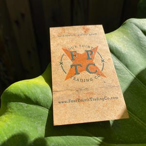 May include: A rectangular tan business card featuring the text hand crafted, quality goods at the top. The centre displays an orange star graphic with the letters FPTC and the text FOUR POINTS TRADING CO. The website www.FourPointsTradingCo.com is printed at the bottom.