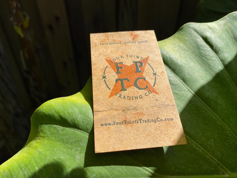 May include: A rectangular tan business card featuring the text hand crafted, quality goods at the top. The centre displays an orange star graphic with the letters FPTC and the text FOUR POINTS TRADING CO. The website www.FourPointsTradingCo.com is printed at the bottom.